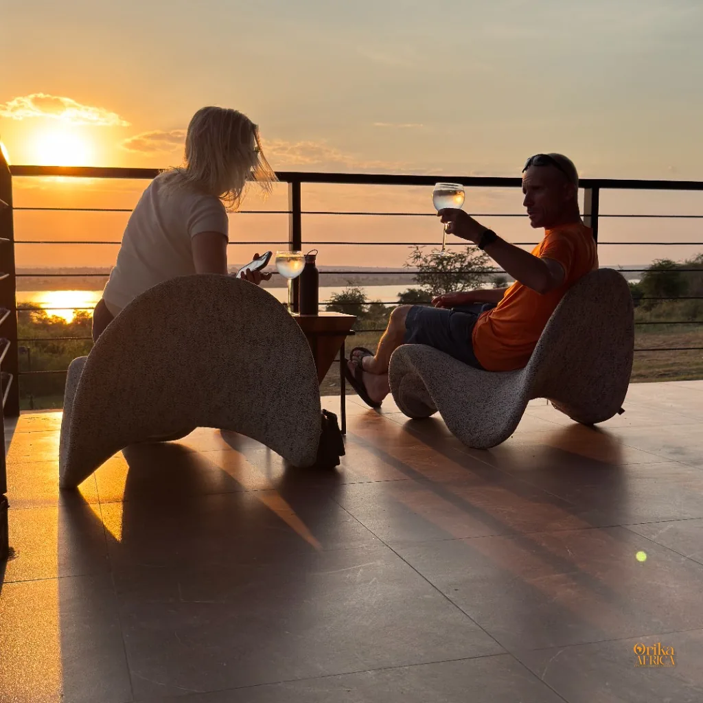 Couple enjoying a sundowner on a luxury safari lodge terrace as the sun sets over the East African wilderness